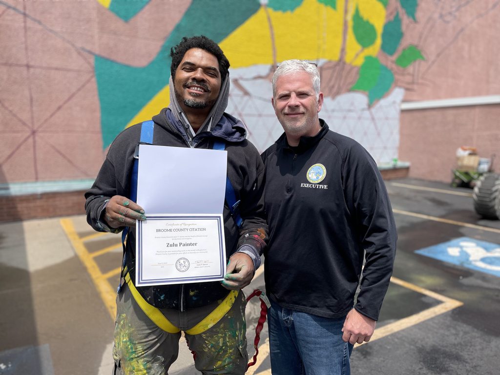 Zulu Painter (left) is presented with a certificate of recognition for his mural by Broome County executive Brian Garner (right).