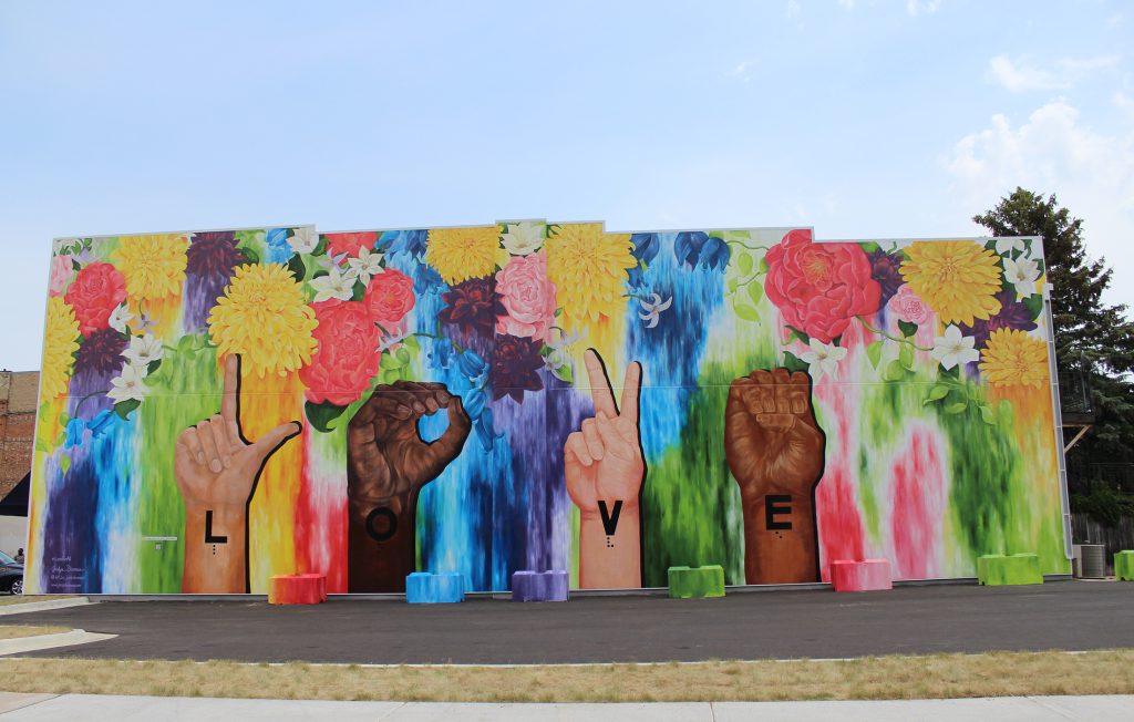 Love For All, 2021, Golden Mural Acrylic Paint and Varnish on Metal, 85’ x 35’, Faribault, MN.  The hands represent the American Sign Language (ASL) alphabet and the Braille letters spell out “love” paying tribute to the Minnesota State Academies for the Deaf & Blind (MSAB/D). Collaborating with MSAB/D, a QR code accessing an ASL video, audio description and Braille plaque was created for the mural.